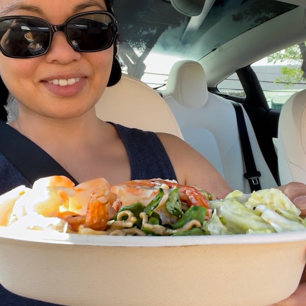 Woman in sunglasses holding up a plate of garlic shrimp