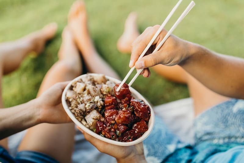 People eating fresh poke out of a bowl with chopsticks