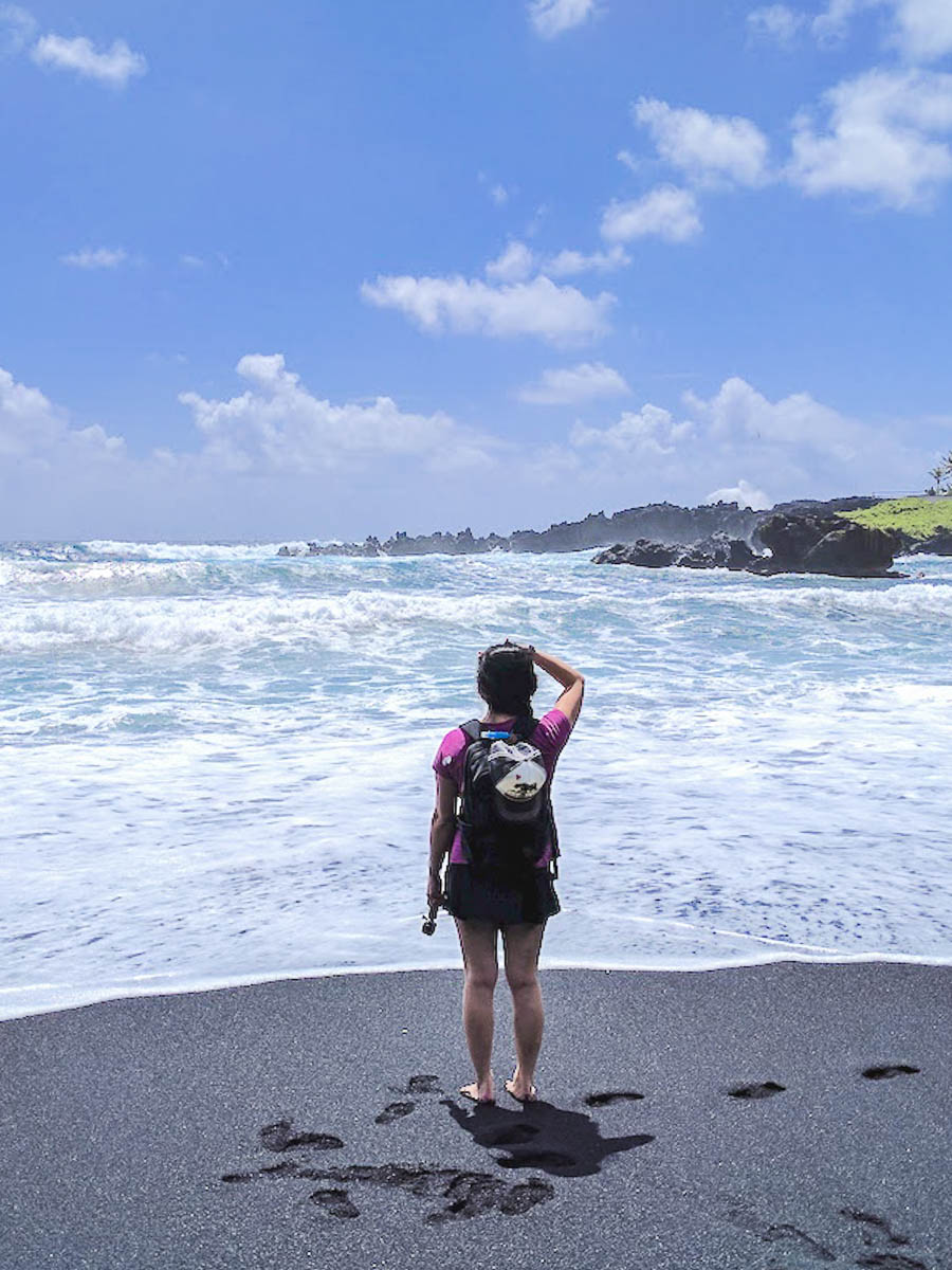 woman standing on a black sand beach and staring at the ocean