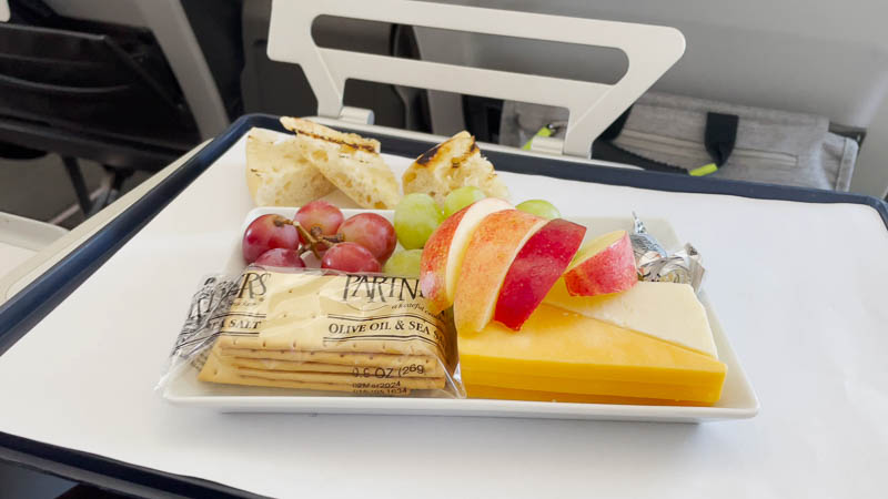 A plate of cheese, crackers, sliced apple, and grapes.