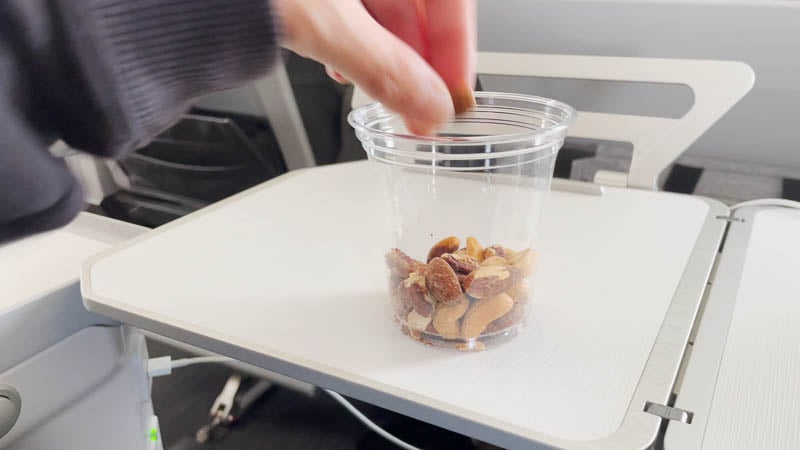 Clear plastic cup partially filled with nuts. A hand picking up with a piece.