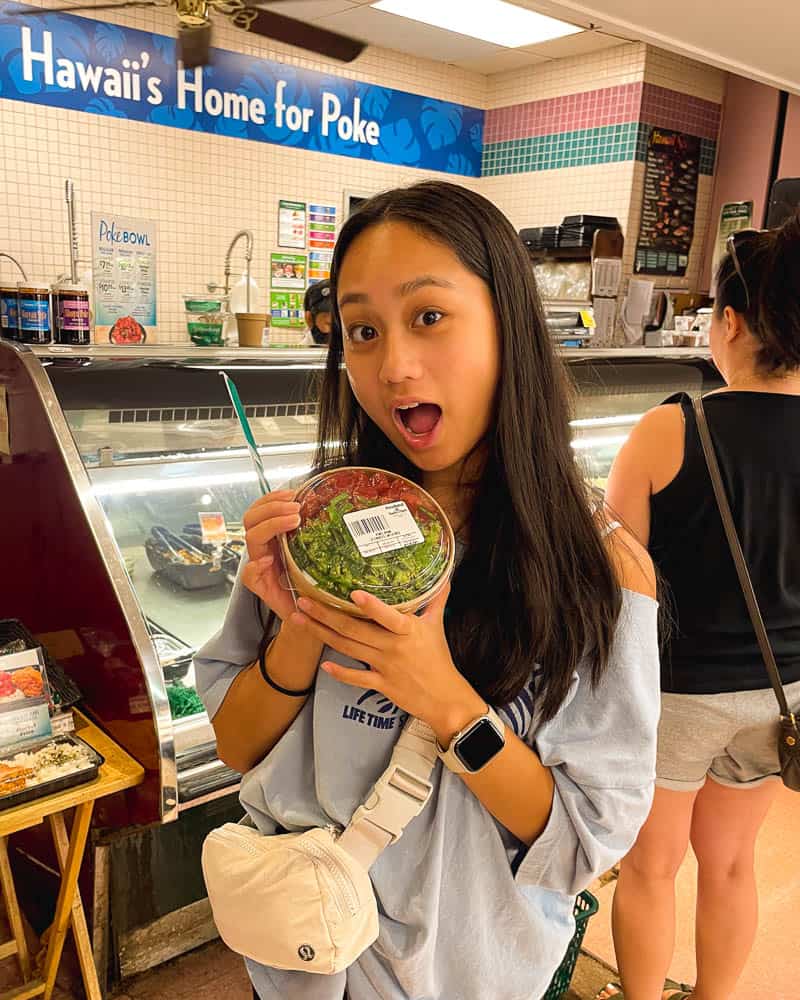 Young woman holds up a bowl of poke at Foodland in Kihei, Maui