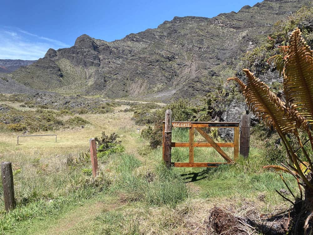 A wooden gate and fence with a green valley in the foreground and mountains in the background.