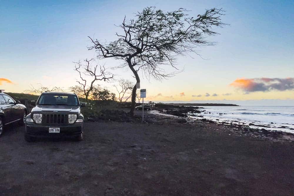 Jeep vehicle parked on the dirt parking lot at La Perouse Bay, Maui next to the water and a silhouette of a tree