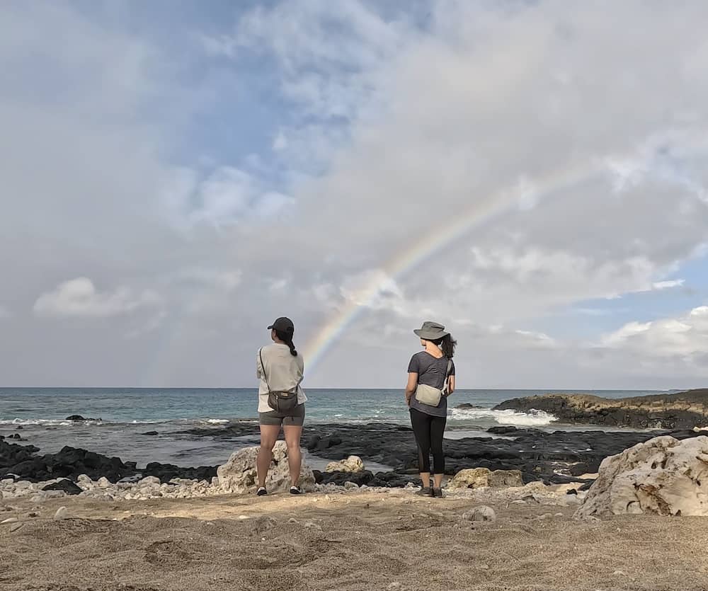 Two women at La Perouse Bay in South Maui looking out from shore with a rainbow in the distance