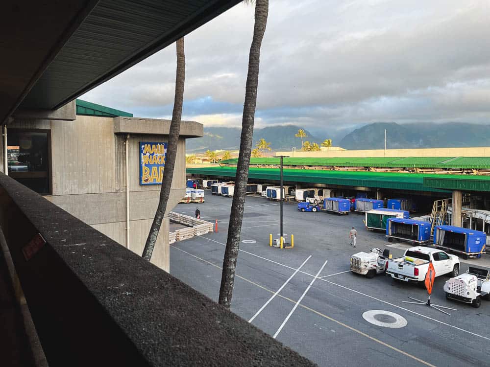 View of baggage carts in the foreground with mountains in the distance from the main terminal at Maui's Kahului Airport