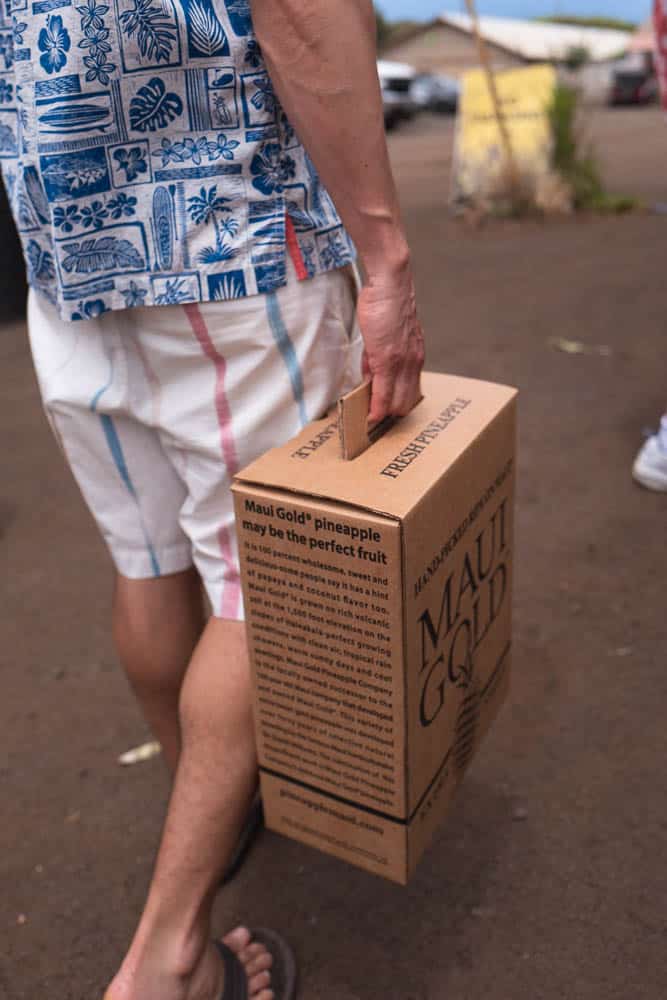 A man carries a branded cardboard box containing two Maui Gold pineapples