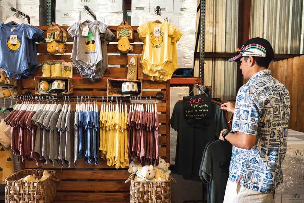 A rack of children's onesies at the Maui Gold Pineapple tour gift shop