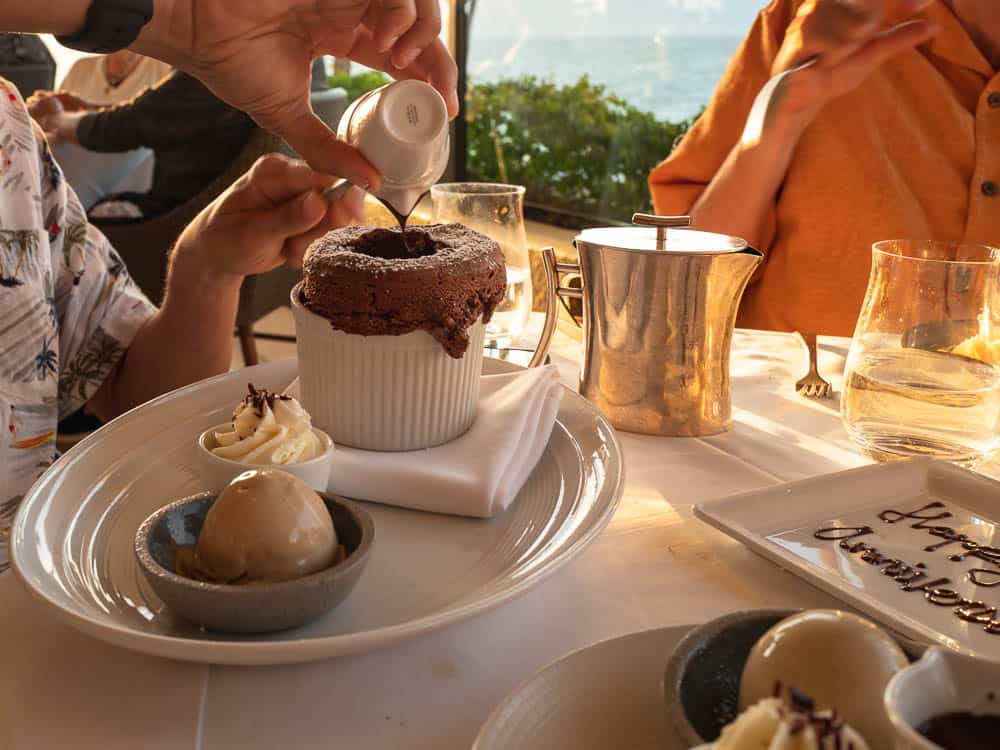 A hand pours chocolate sauce onto a chocolate souflee dessert at Spago at The Four Seasons Wailea, Maui