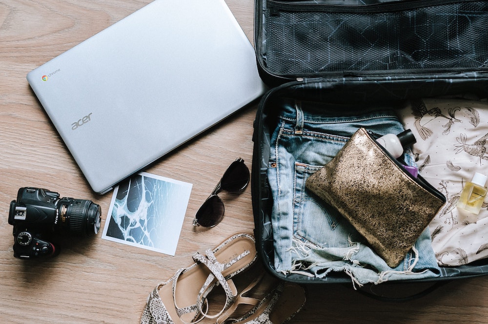 Laptop, DSLR camera, sunglasses next to an open suitcase